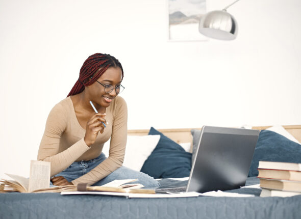 Young teenage girl sitting on her bed studying and using a lapto